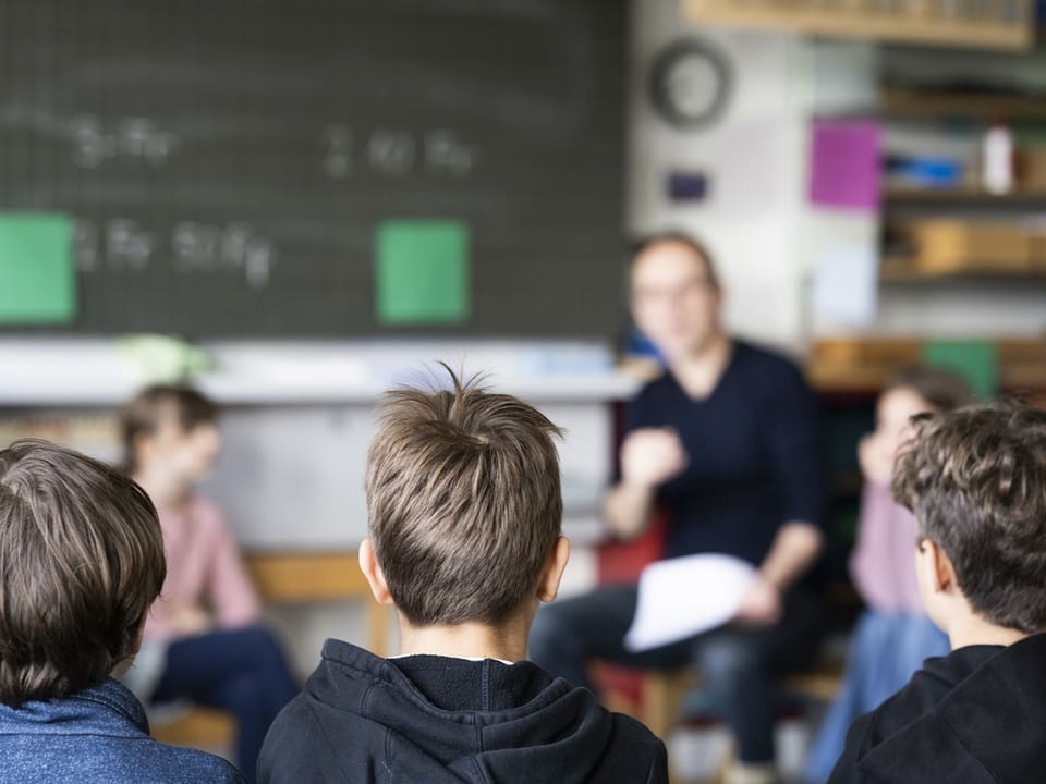 Kinder im Klassenzimmer hören einem Erwachsenen zu.