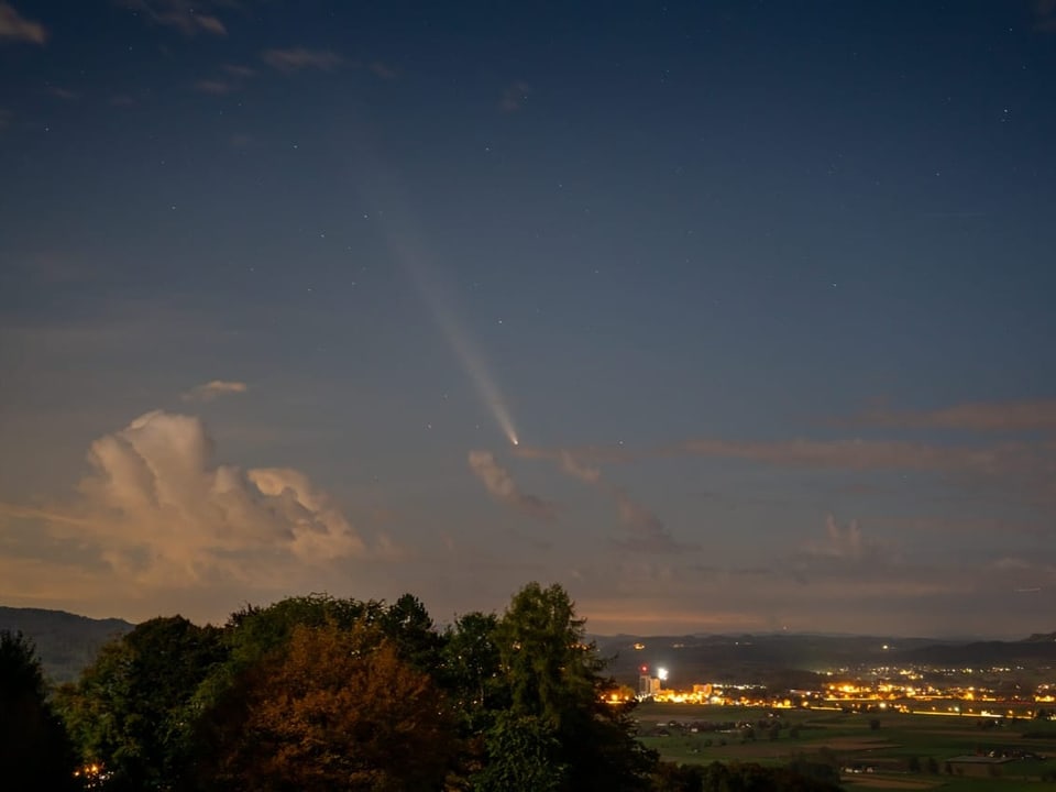 Nachtlandschaft mit Komet über beleuchteter Stadt.