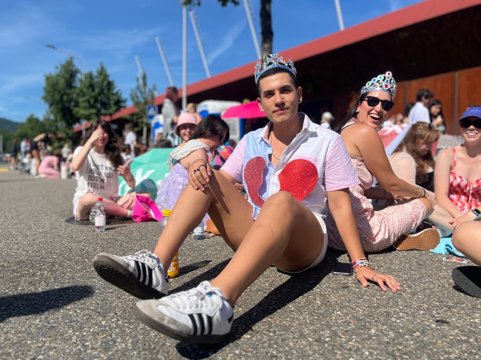 Fans von Taylor Swift sitzen vor dem Stadion am Boden und warten auf das Konzert.