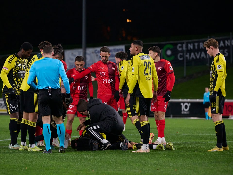 Spieler umringen verletzten Fussballspieler auf dem Feld.