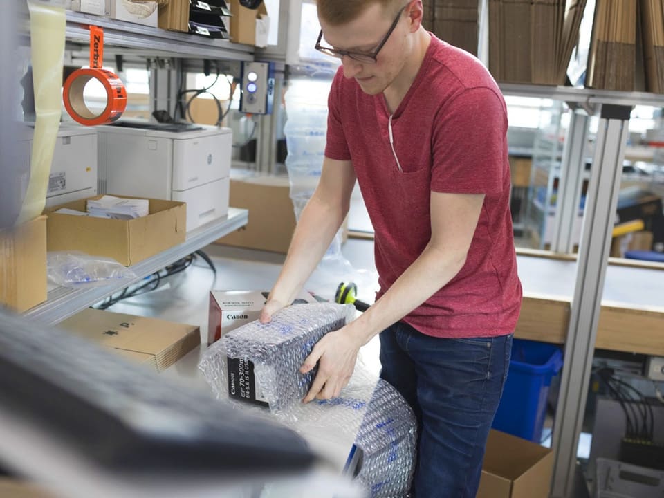 Mann in rotem Shirt packt ein Paket im Büro aus.