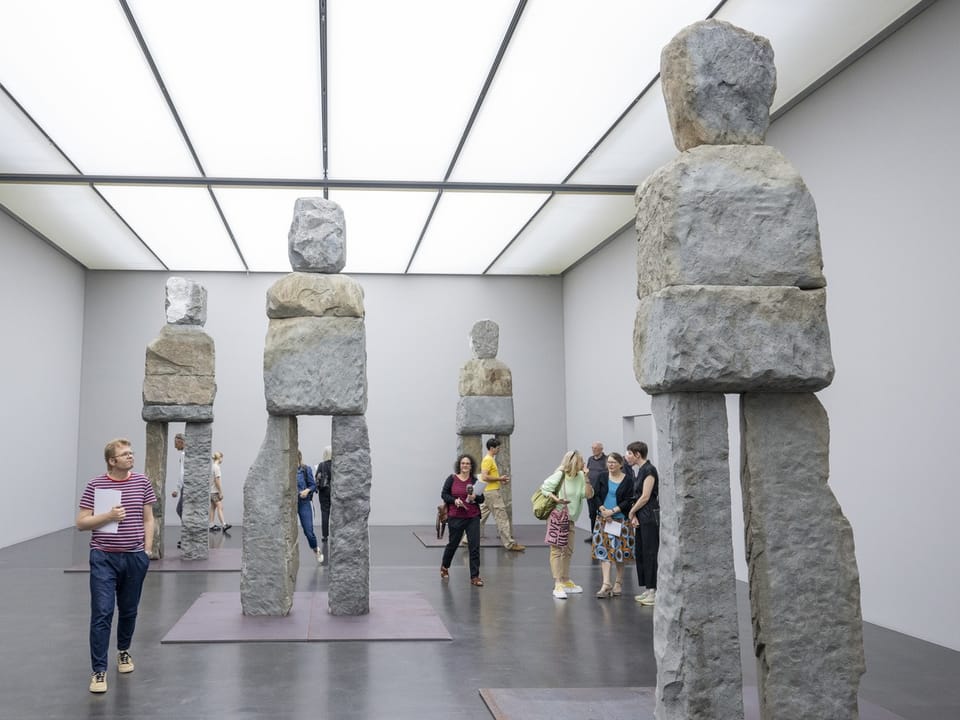 Menschen betrachten Steinskulpturen in einer Galerie.