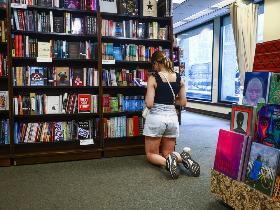 Frau kniet in einer Buchhandlung vor Bücherregal.