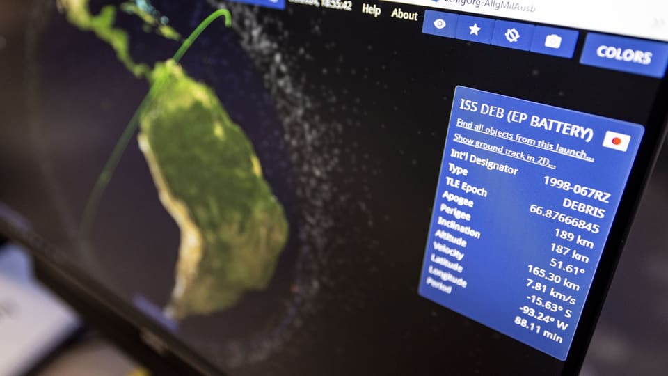 Auf einem Monitor wird die Flugbahn eines ausrangierten Batteriepakets der ISS um die Erde angezeigt, dazu Daten 