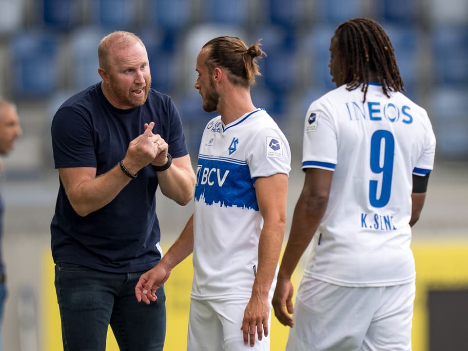 Trainer spricht mit zwei Fussballspielern im weissen Trikot.