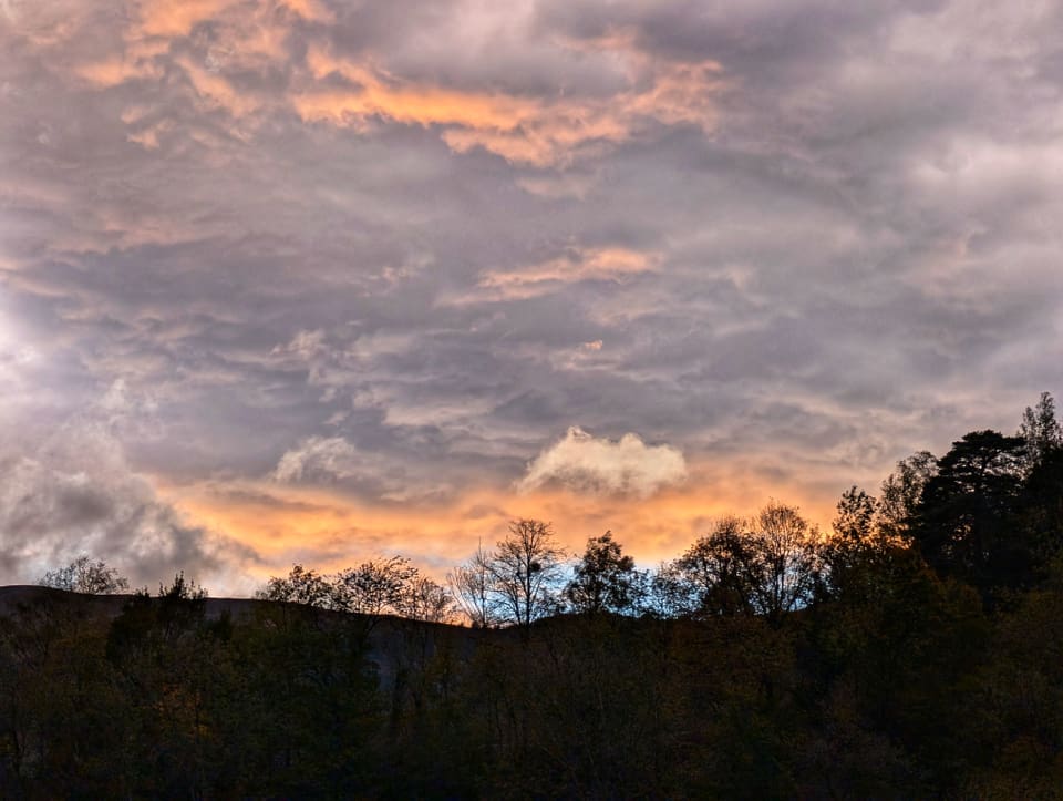 Dramatischer Himmel mit Wolken über Silhouetten von Bäumen bei Sonnenuntergang.