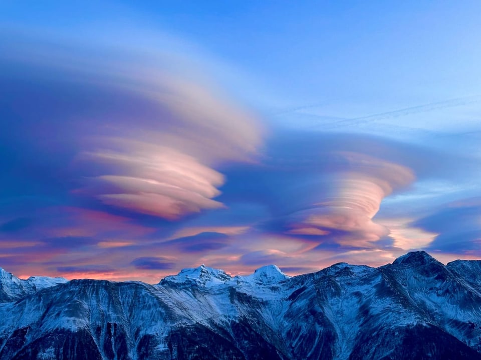 Lenticulariswolken über schneebedeckten Bergen bei Sonnenuntergang.