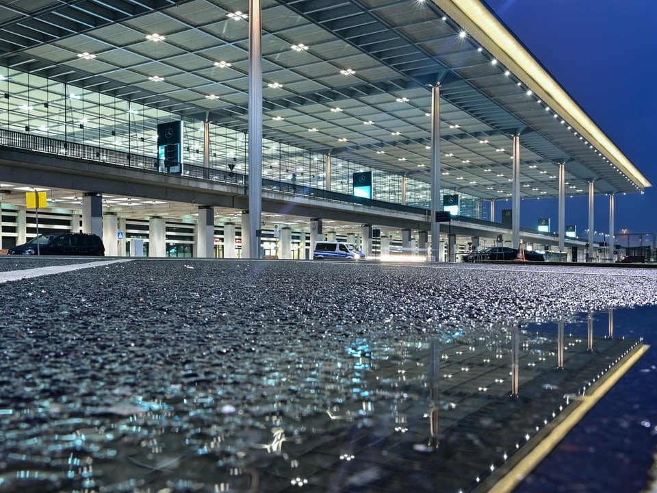 Aussenansicht des Terminal 1, beleuchtet, im Regenwetter.