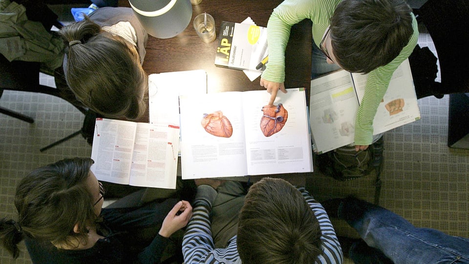 Sicht auf einen Arbeitstisch von Medizinstudenten vor einem offenen Anatomiebuch.