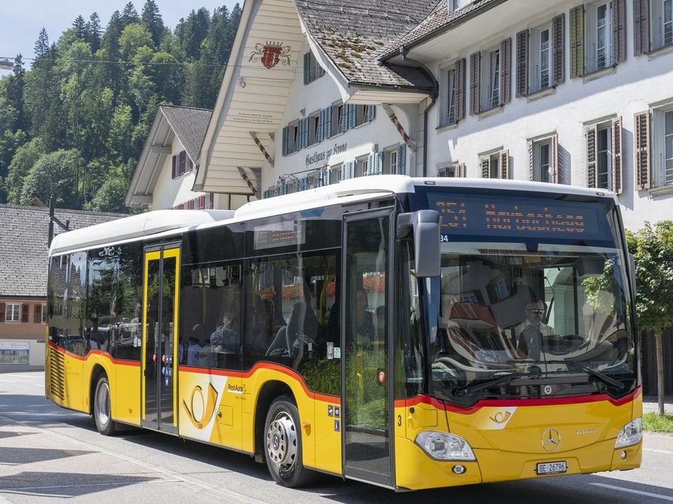 Gelber Postbus vor traditionellem Schweizer Gebäude.