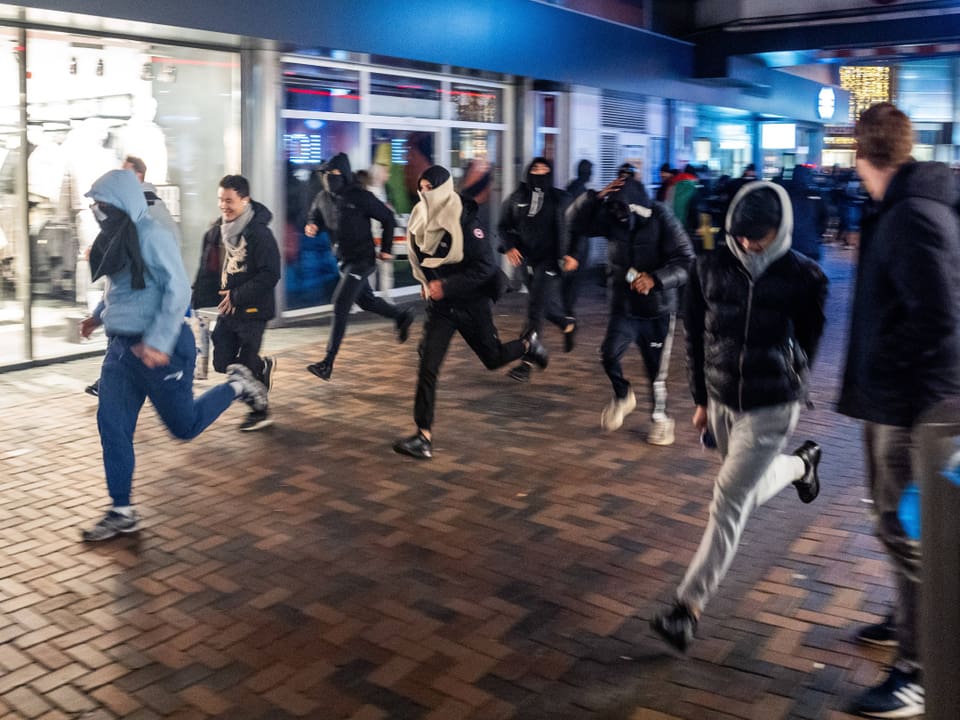 Menschen rennen in einer Einkaufsstrasse bei Nacht.