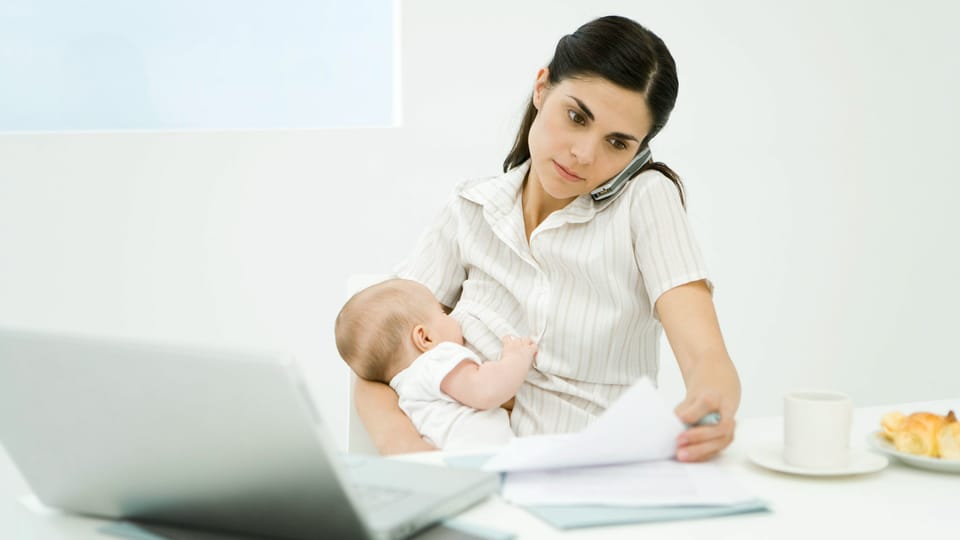 Frau mit Baby im Arm vor Computer.