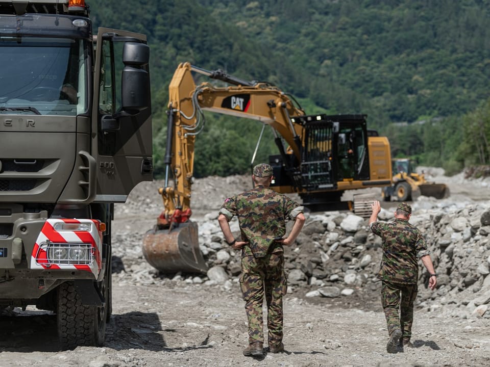 Zwei Soldaten und schwere Maschinen an einer Baustelle im Wald.