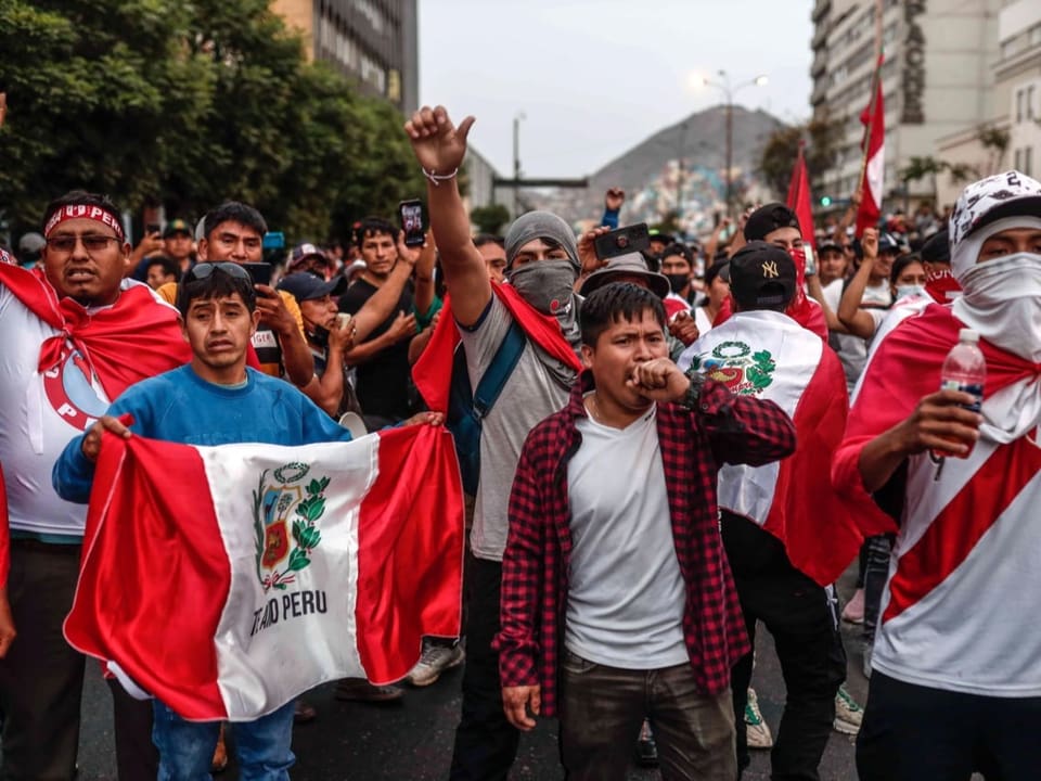 Eine Menschenmenge steht auf der Strasse. Sie tragen peruanische Flaggen und rufen Parolen.