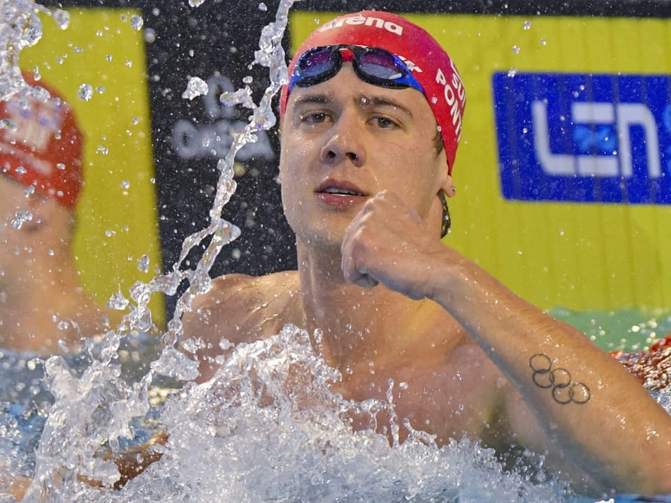 Schwimmer jubelt im Wasser mit roter Badekappe und gestrecktem Arm.