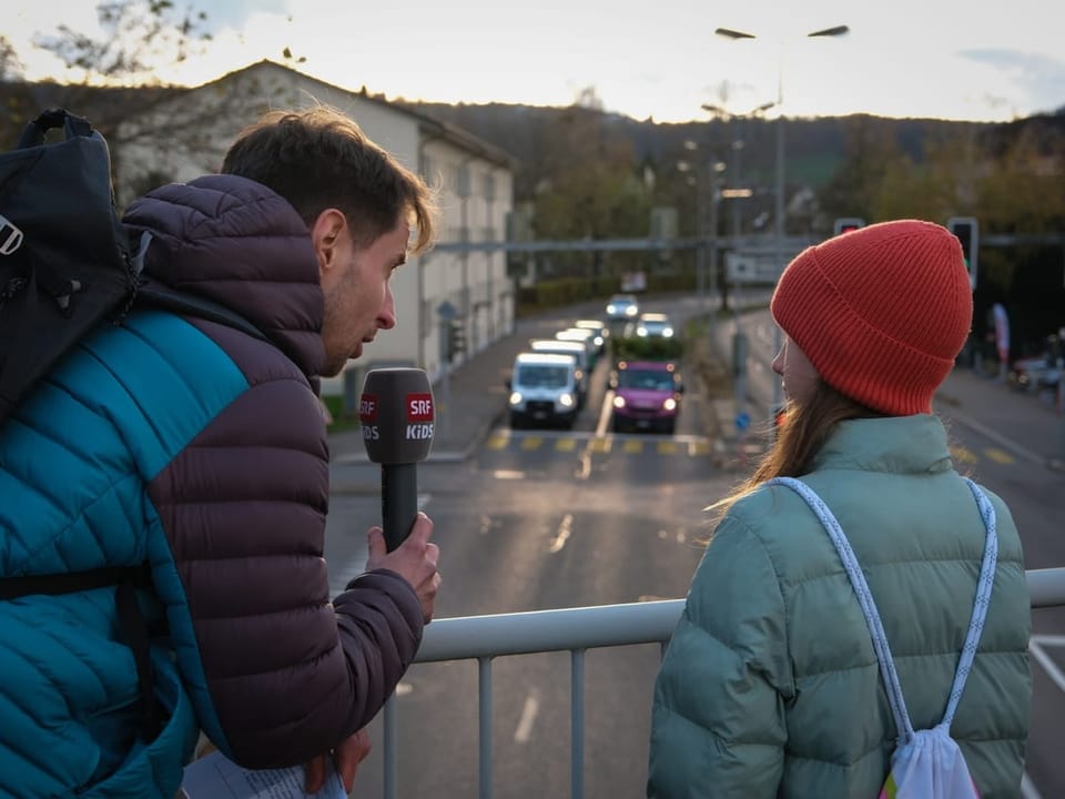 Zwei Menschen stehen an einem Geländer. Unter ihnen fahren viele Autos auf einer vierspurigen Strasse. 