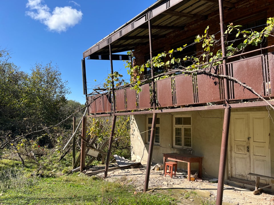 Altes, verwittertes Gebäude mit Balkon in ländlicher Umgebung.