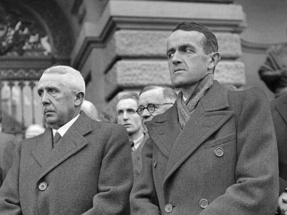 Schwarzweissaufnahme: Zwei Männer in Mänteln posieren vor dem Bundeshaus