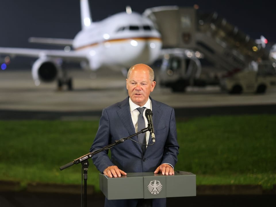 Mann hält Rede vor Flugzeug auf dem Rollfeld.