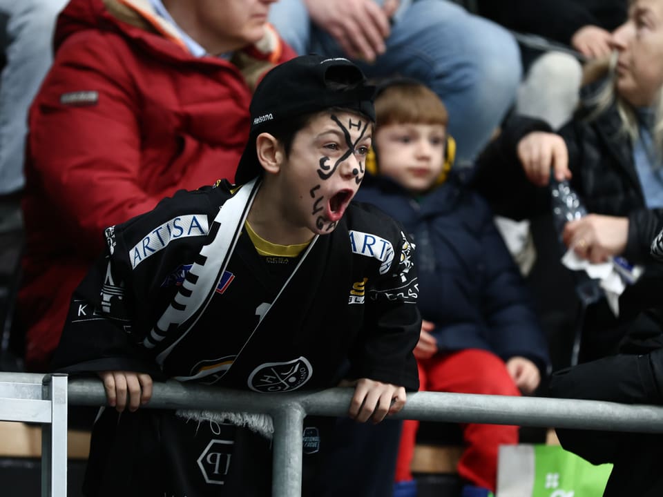 Kind mit bemaltem Gesicht schreit in einem Sportstadion.