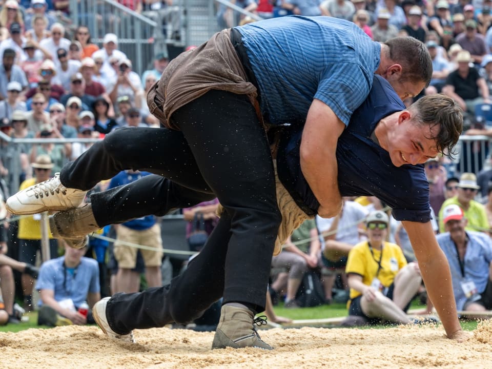 Zwei Männer ringen in einem Sandring vor einer Menschenmenge.