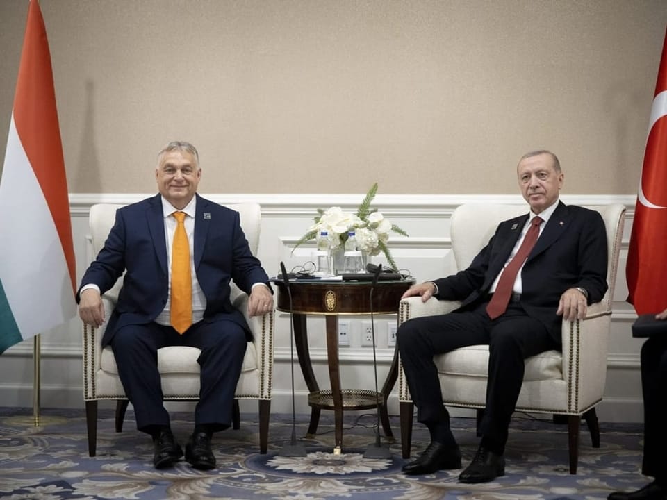 Zwei Männer sitzen neben Flaggen Ungarns und der Türkei.