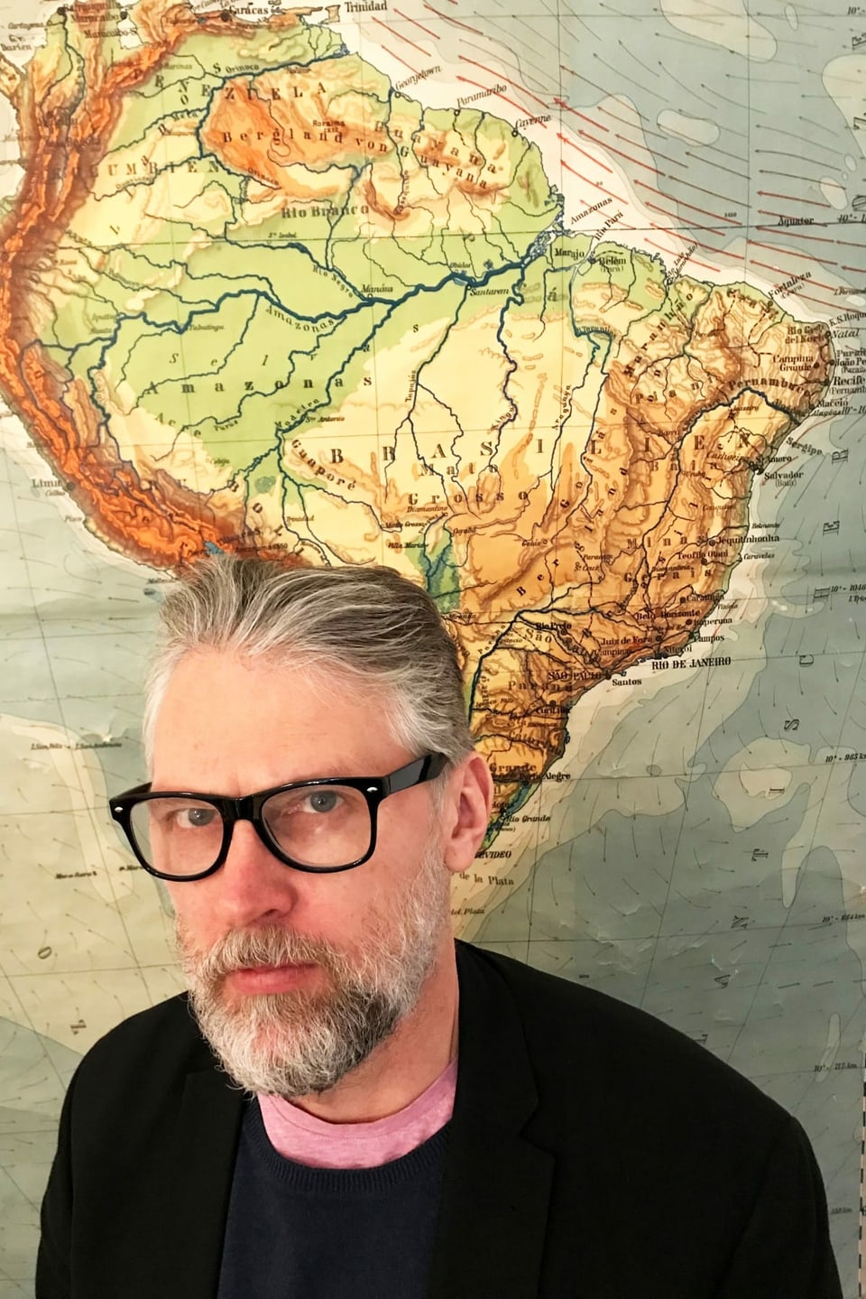 Mann in schwarzem Pullover vor Landkarte Südamerikas