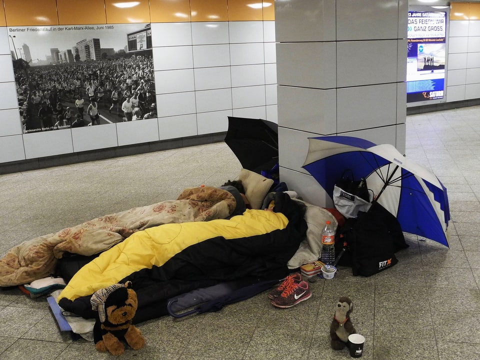 Zwei Personen in Schlafsäcken liegen in einer Unterführung.