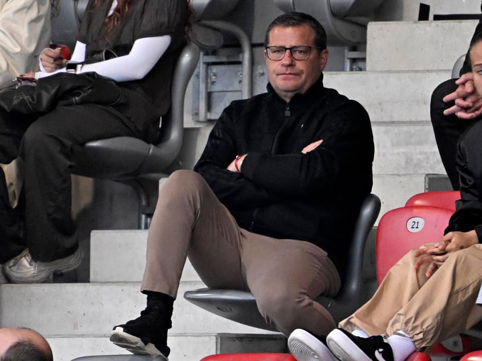 Mann mit verschränkten Armen sitzt auf Stadiontribüne.