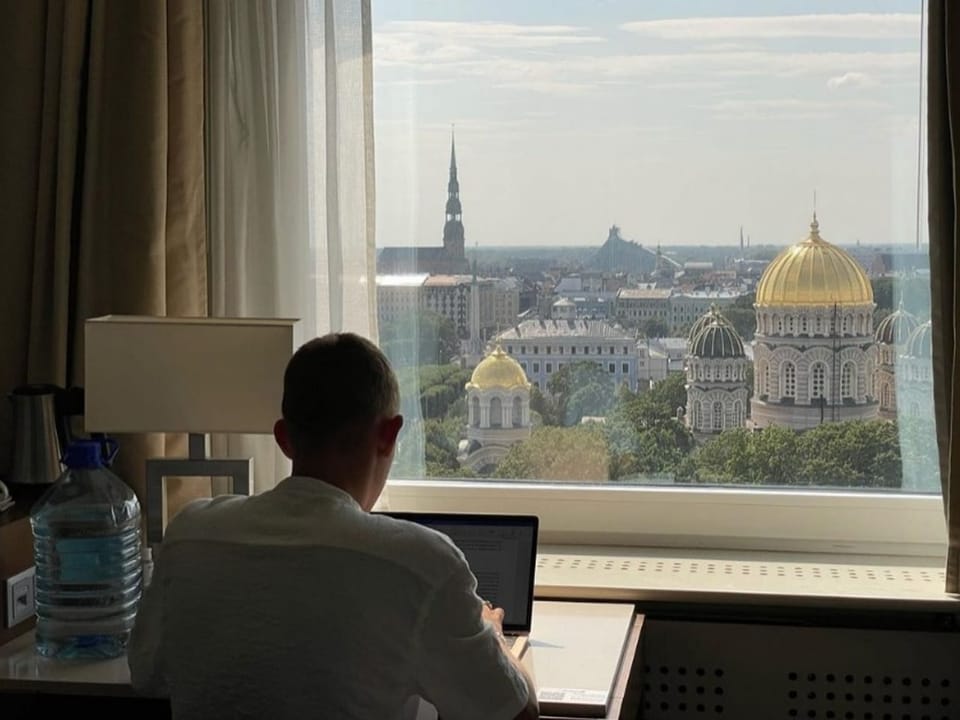 Mann sitzt am Laptop und schaut aus dem Fenster auf die Stadt Riga. 