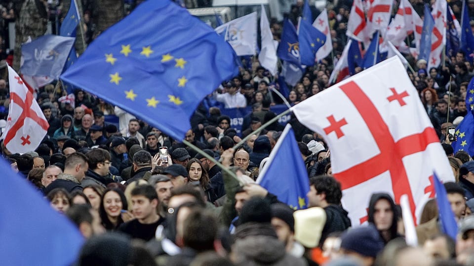 Menschenmenge schwenkt EU- und georgische Flaggen bei einer Demonstration.