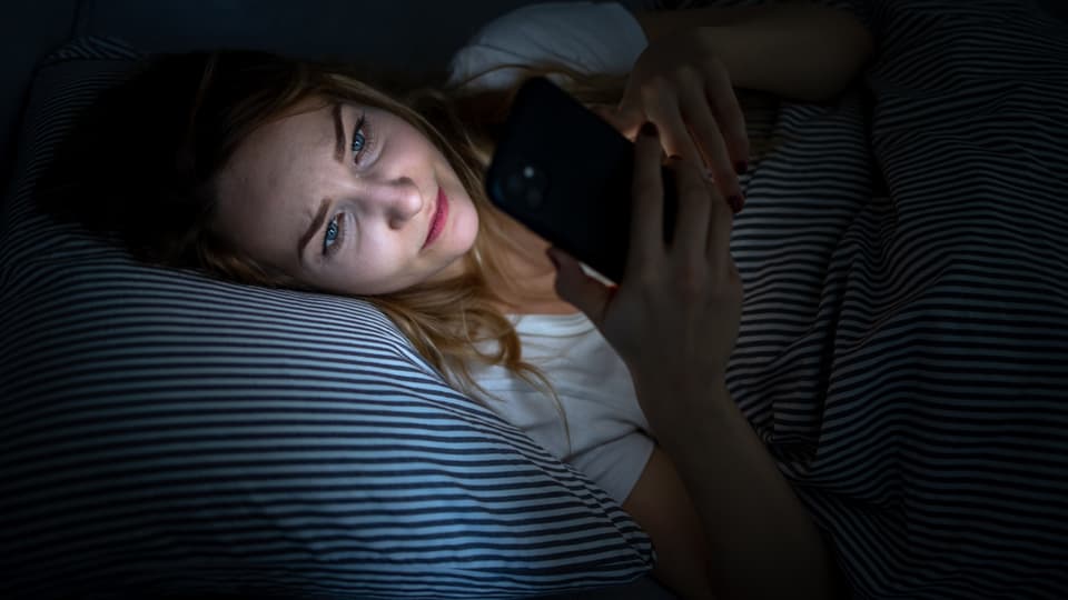 Frau in Bett, ihr Gesicht wird vom Handy angeleuchtet