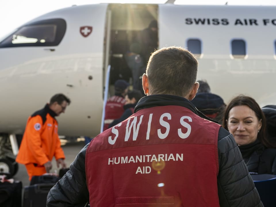 Schweizer Humanitäre Hilfe neben Flugzeug mit Swiss Air Force Kennzeichnung.