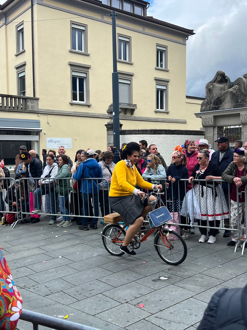 Person fährt Fahrrad bei einer Strassenparade, von Menschen am Strassenrand beobachtet.