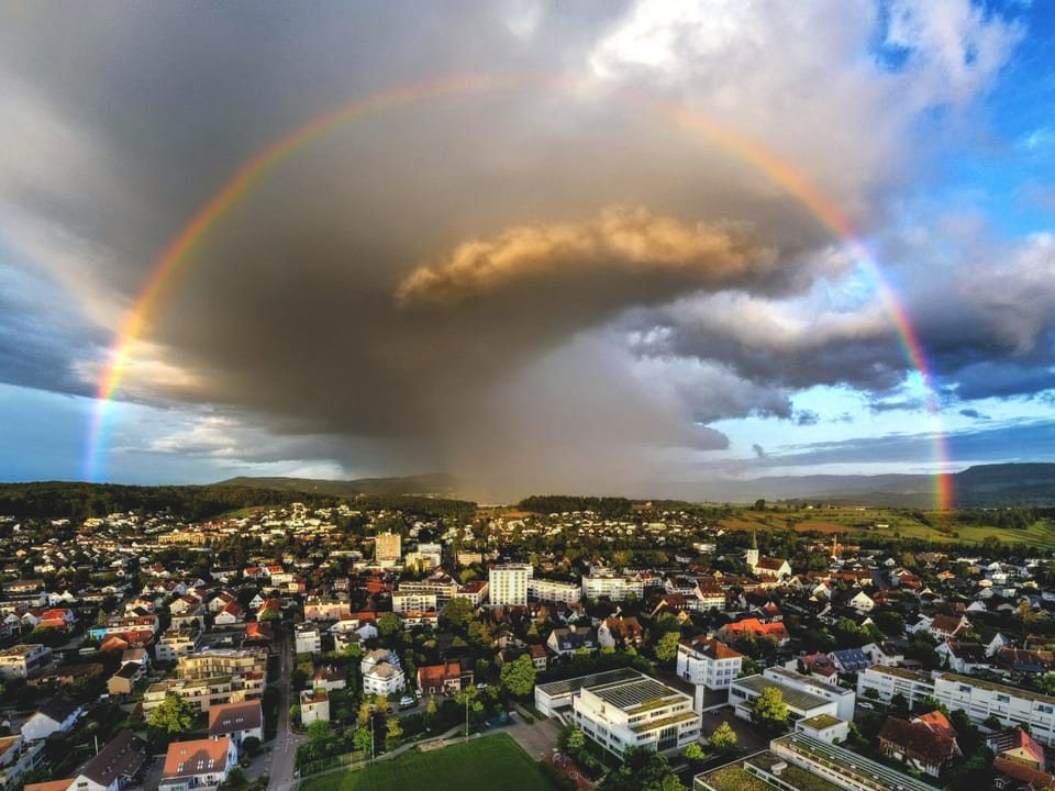 Blick auf Regenbogen und Gewitterzelle über Stadt.