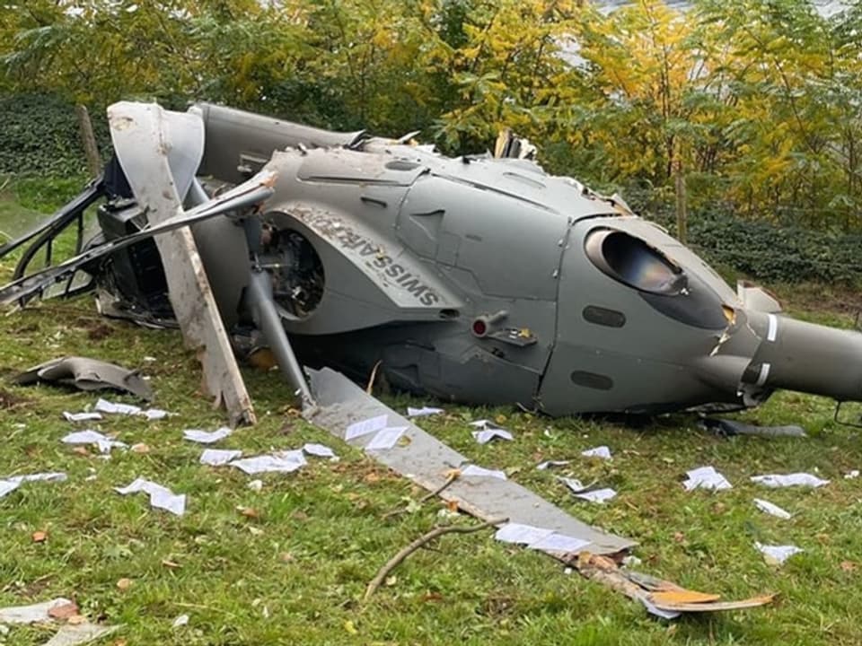 Helikopterwrack auf Wiese mit verstreuten Papieren.