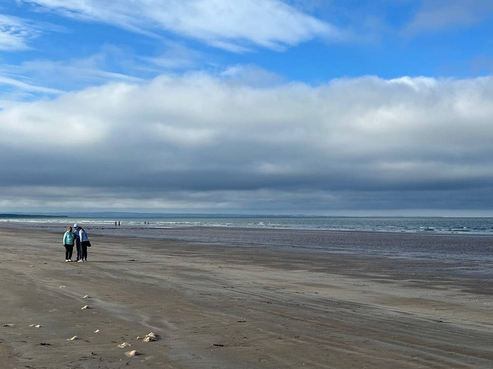 Menschen spazieren am Strand unter bewölktem Himmel.