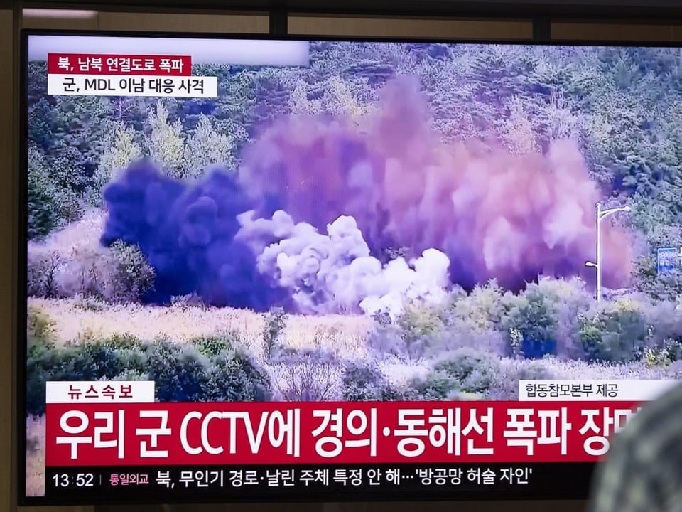 Fernsehbildschirm zeigt Explosion in bewaldetem Gebiet mit koreanischem Text.