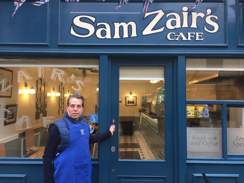 Mann in blauer Schürze steht vor Sam Zair's Café.