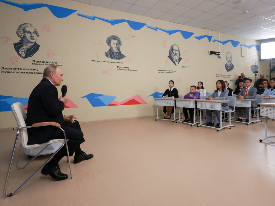 Der russische Präsident Wladimir Putin sitzt vor Schülerinnen und Schülern in einem Klassenzimmer