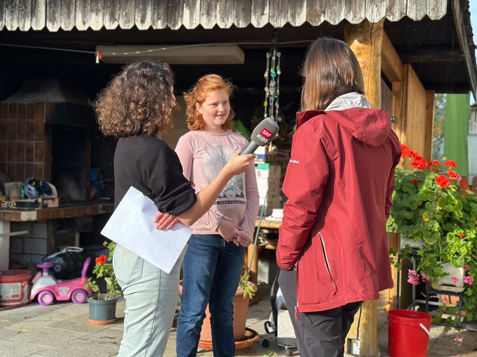 Zwei Frauen und ein Kind unterhalten sich. Eine Frau hält ein Mikrofon von SRF Kids. 