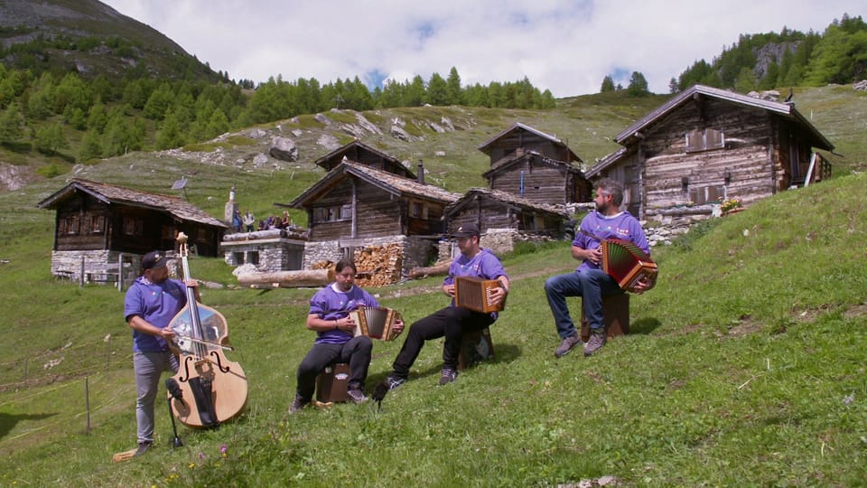Band sitzt auf Alp vor Holzhütten  und musiziert in Sennenchutteli.