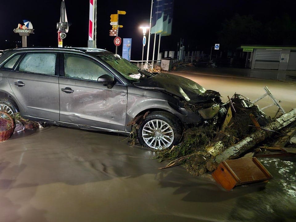 Beschädigtes Auto in überfluteter Strasse bei Nacht.