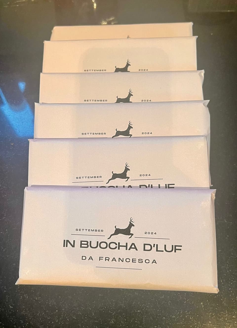 Sechs Schokoladenverpackungen mit der Aufschrift 'IN BUOCHA D'LUF DA FRANCEScA' in einer Reihe.