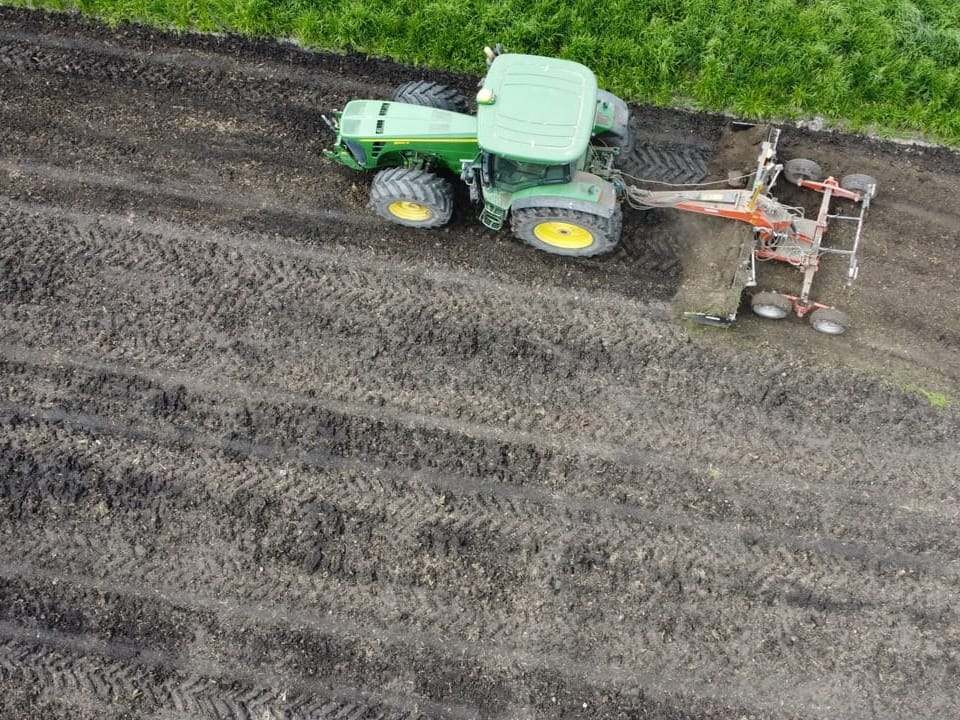 Luftaufnahme eines Traktors, der ein Feld pflügt.