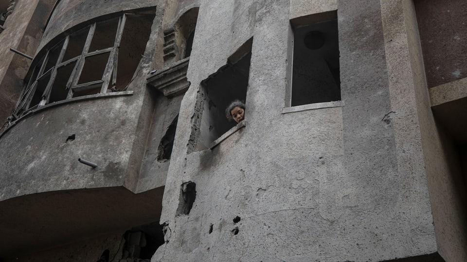 Eine junge Frau schaut aus einem zerstörten Haus in Gaza zum Fenster hinaus