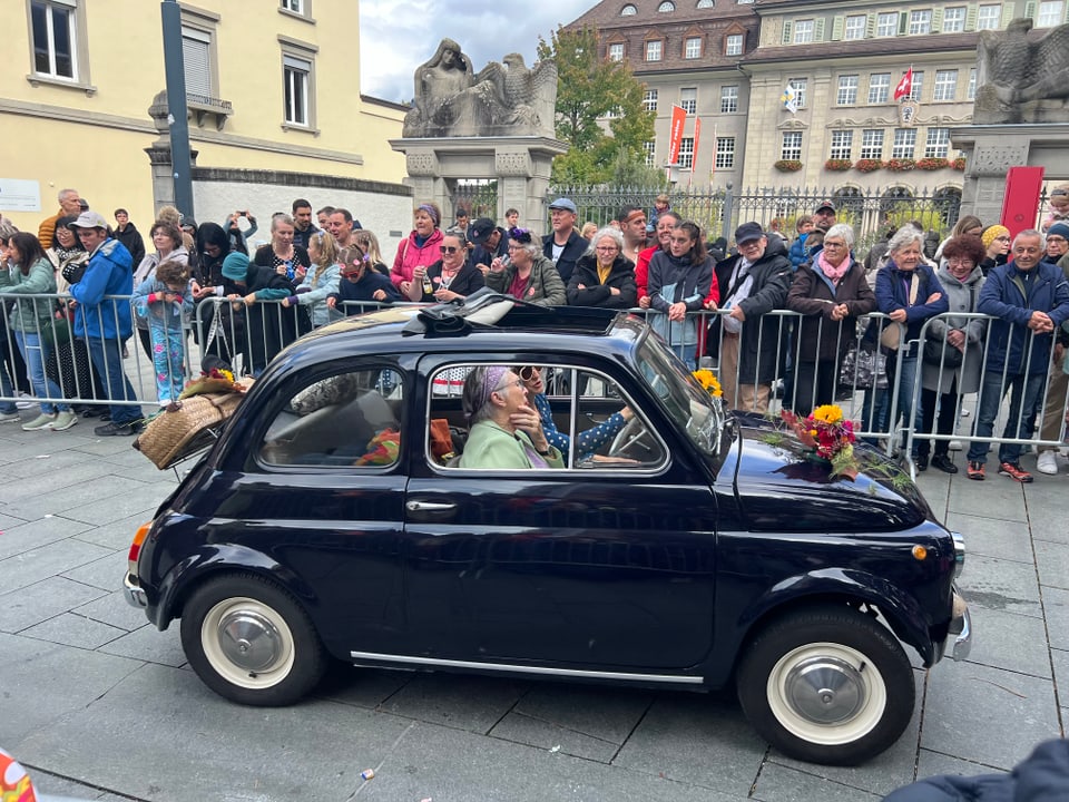 Schwarzes Auto bei Parade, Zuschauer hinter Absperrung.