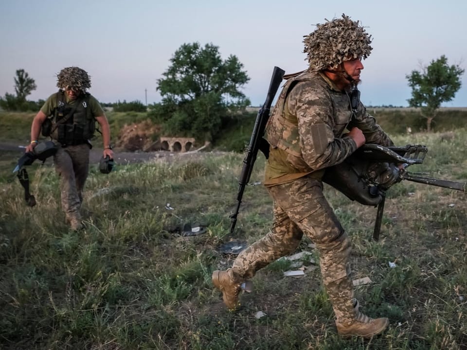 Zwei Soldaten tragen Ausrüstung auf einem Feld.
