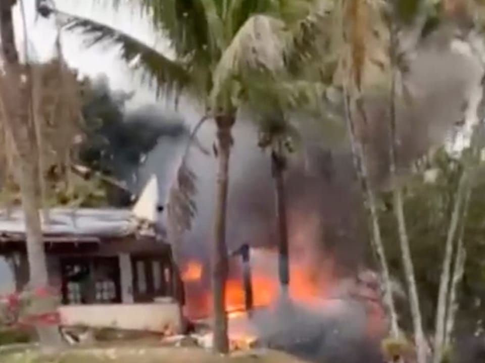 Hausbrand mit Flammen und Rauch, umgeben von Palmen.