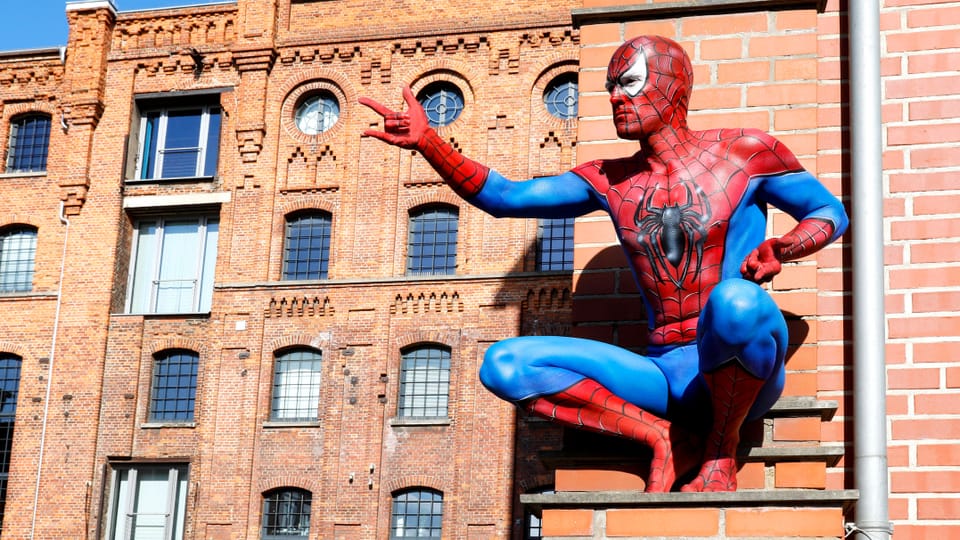 Spiderman sitzt auf einer Leiter vor einem Gebäude aus Backstein.